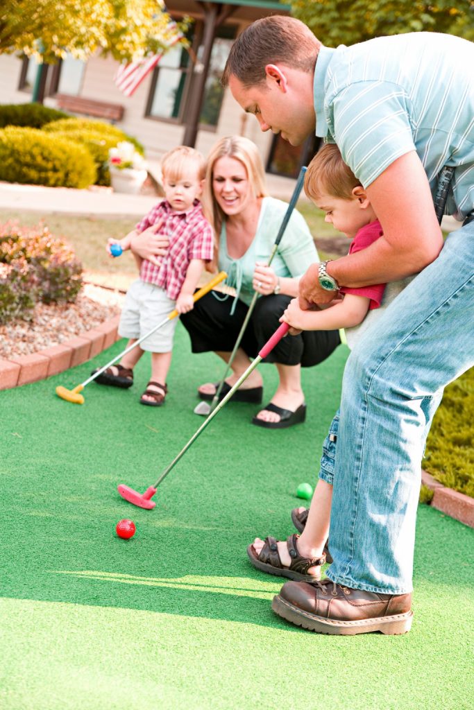 Cute, typical family playing outdoor mini-golf.